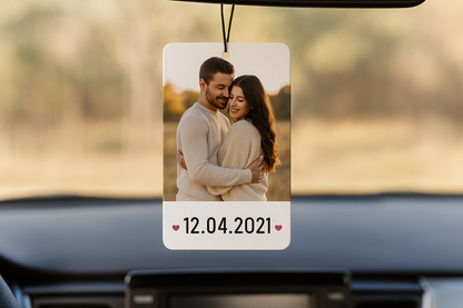 Ambientador de carro retangular, pendurado no espelho retrovisor, com uma foto de um casal de corpo inteiro, abaixo da foto tem um espaço em branco que contém a data 12.04.2021, com um coração vermelho de cada lado da data